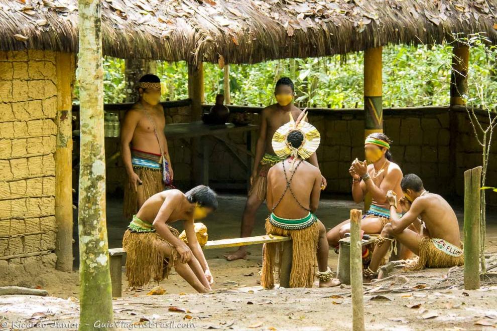 Imagem de vários índios conversando na varanda de uma casa de barro.